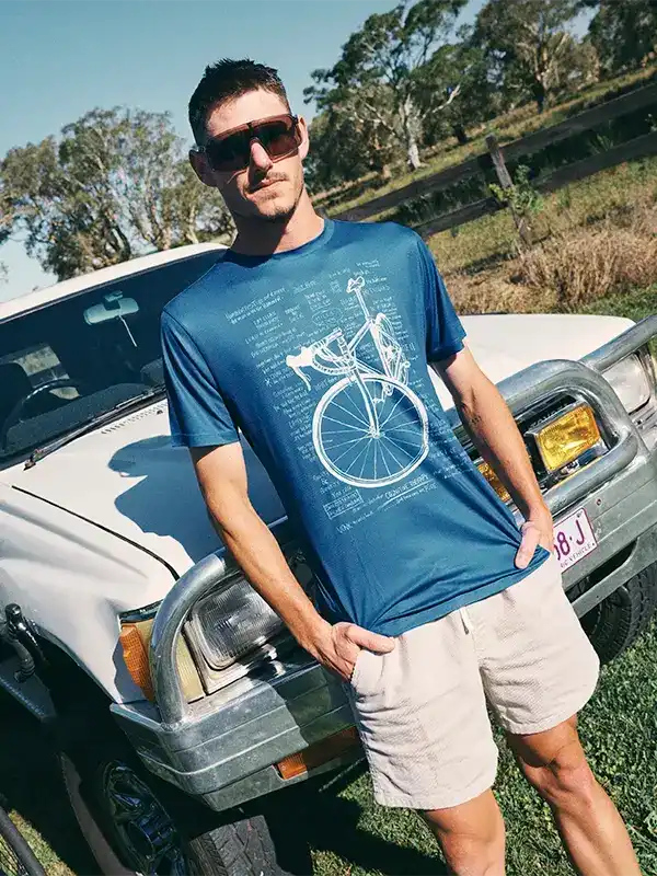 Man wearing blue cycling graphic tee with vintage bike print, standing by truck outdoors