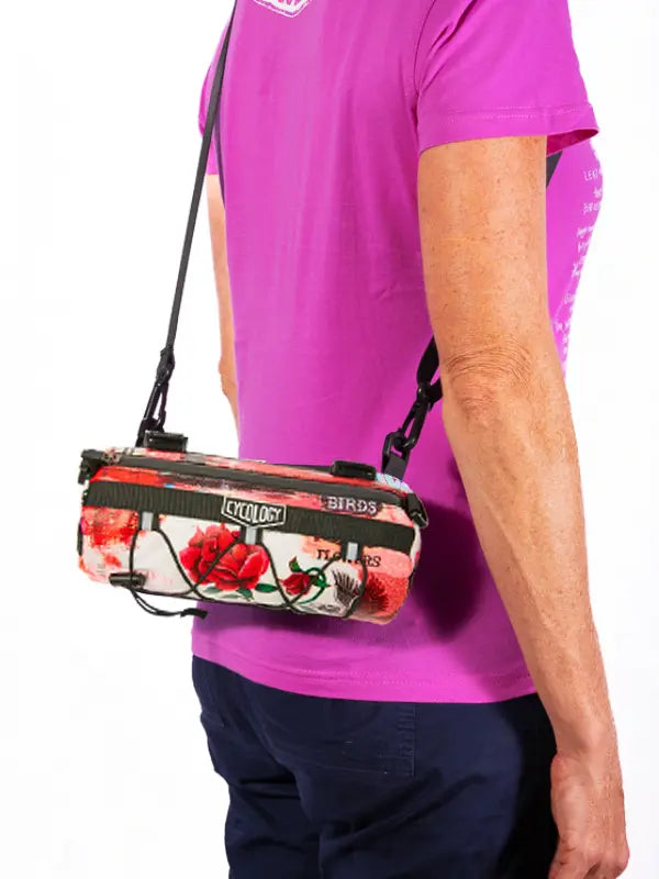 Person wearing a pink shirt with a floral-patterned bike bag over their shoulder on a white background
