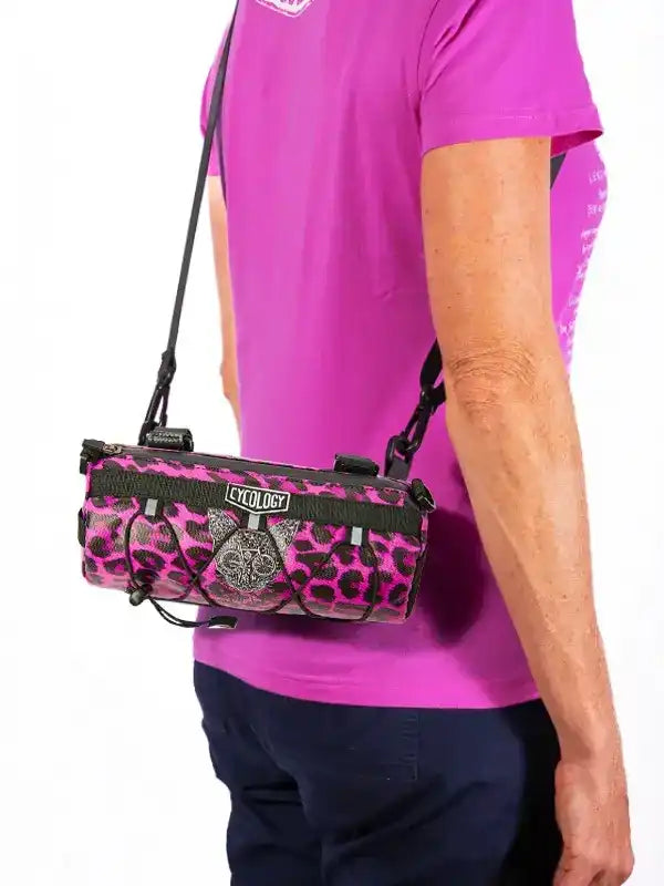Pink leopard print cycling bag with black straps, worn crossbody by person in magenta shirt