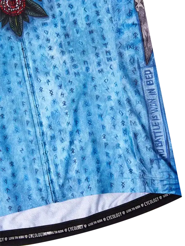 Blue cycling jersey with rune pattern, floral graphic, and 'No Battle Is Won In Bed' text, featuring breathable fabric and branded hem.