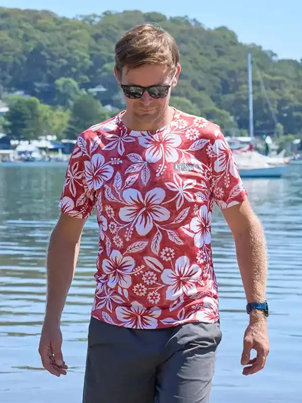 Man wearing red floral print cycling shirt by water, sunglasses, gray shorts