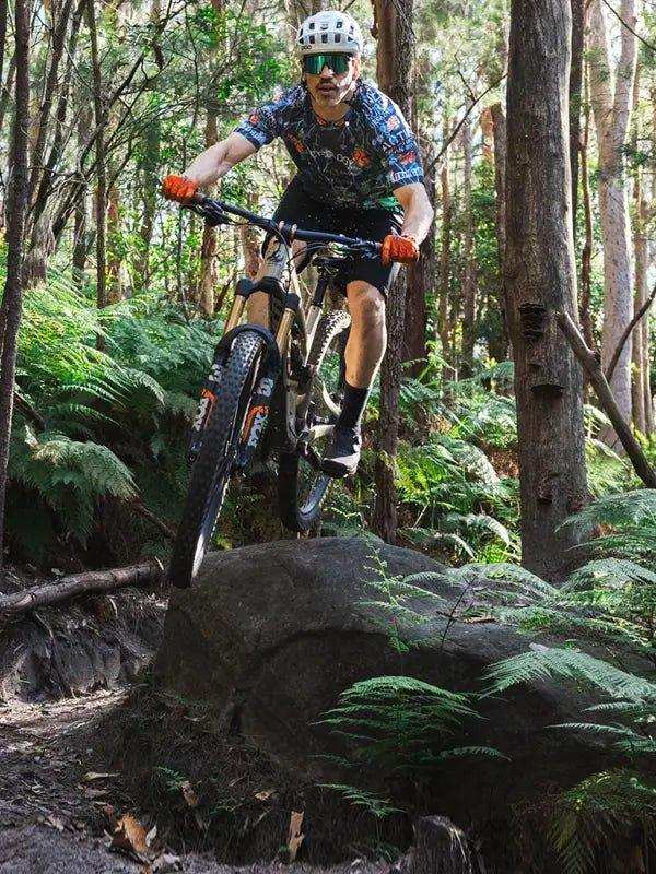 Man mountain biking in forest wearing cycling jersey and helmet, riding over rock trail