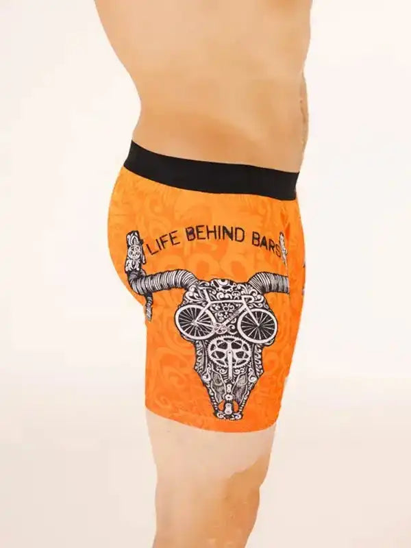 Orange men's cycling shorts with skull and bike graphic, 'Life Behind Bars' text, black waistband