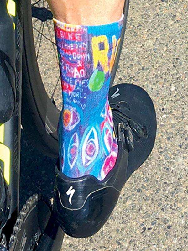 Colorful cycling socks with bold graphics and text, worn with black bike shoes on pavement