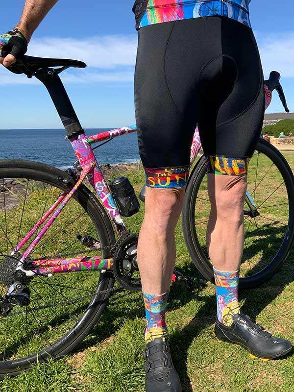 Men's cycling shorts with colorful socks and bike by ocean, featuring padded design and vibrant patterns
