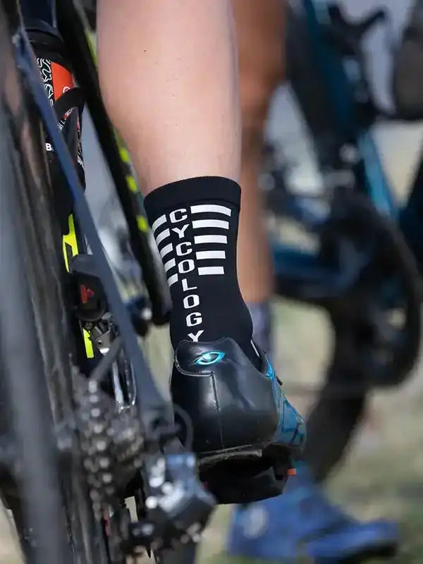 Cycling socks with 'CYCOLOGY' text and stripes, worn with bike shoes on a road bike