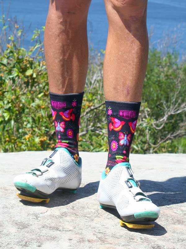 Colorful butterfly-patterned cycling socks with white bike shoes, outdoors near water