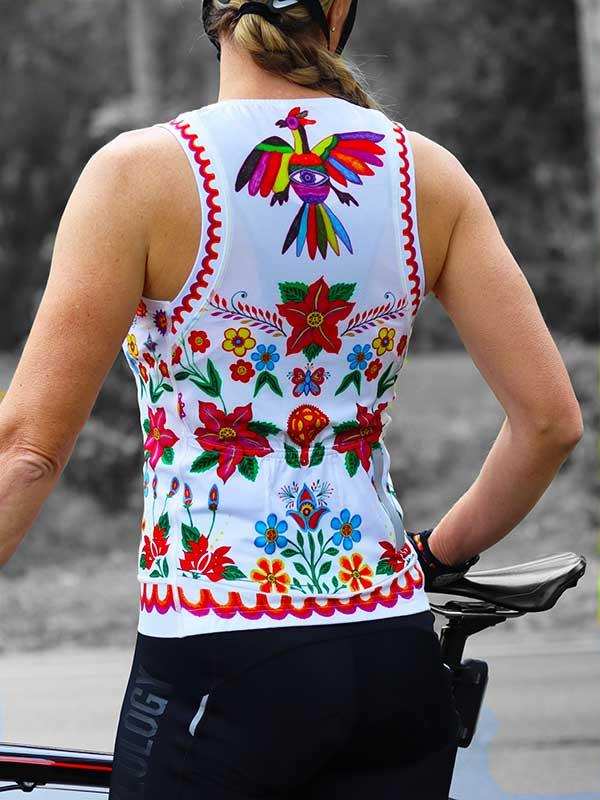 Woman wearing colorful floral and bird patterned cycling jersey, standing by bike