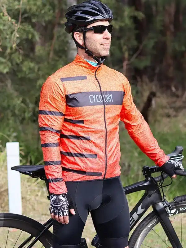Man in orange cycling jersey with black stripes, helmet, and gloves, standing with road bike outdoors