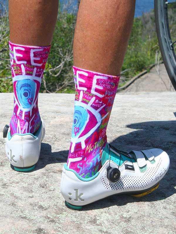 Vibrant pink cycling socks with bold graphic designs, worn with white bike shoes on rocky terrain
