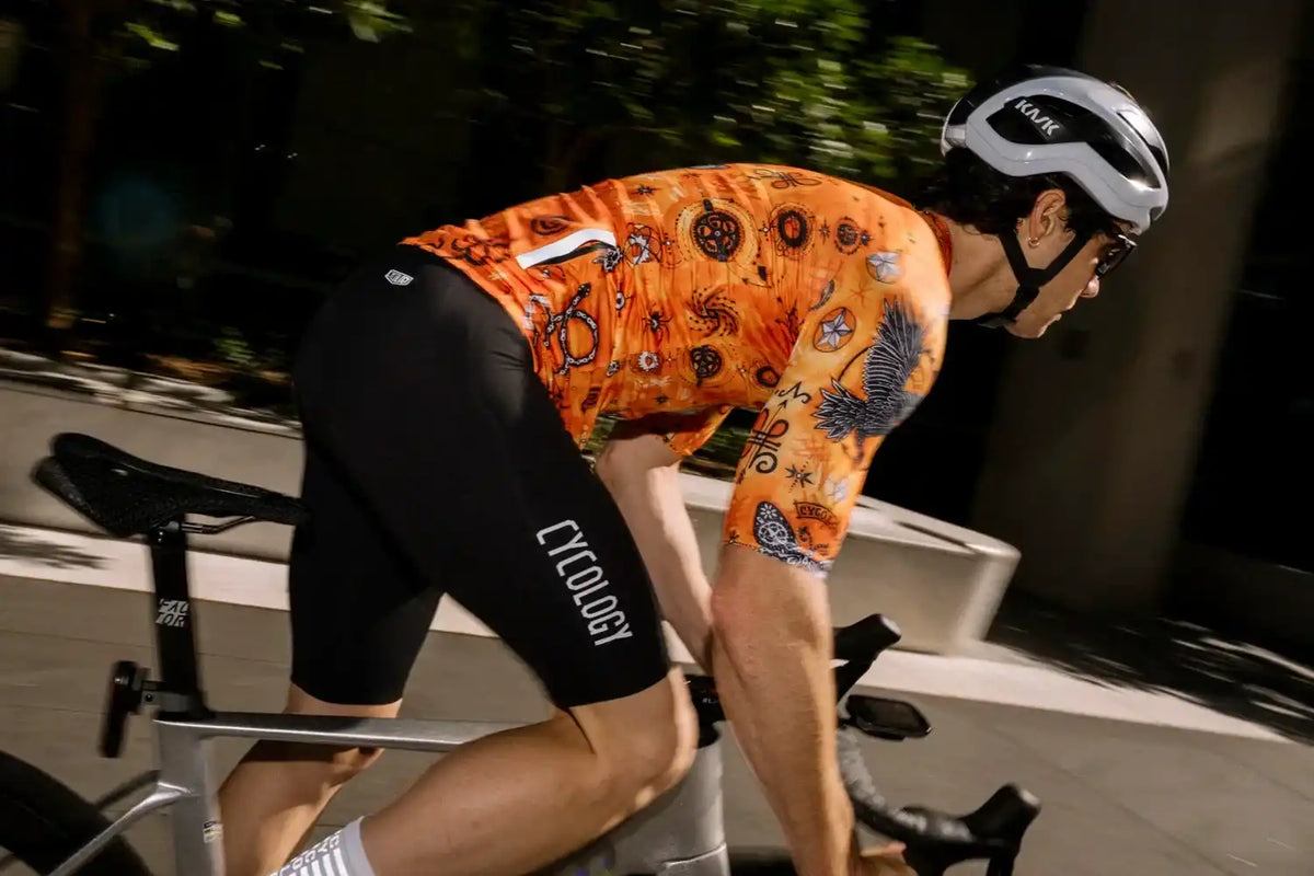 Man cycling in vibrant orange patterned jersey and black Cycology shorts, wearing Kask helmet.