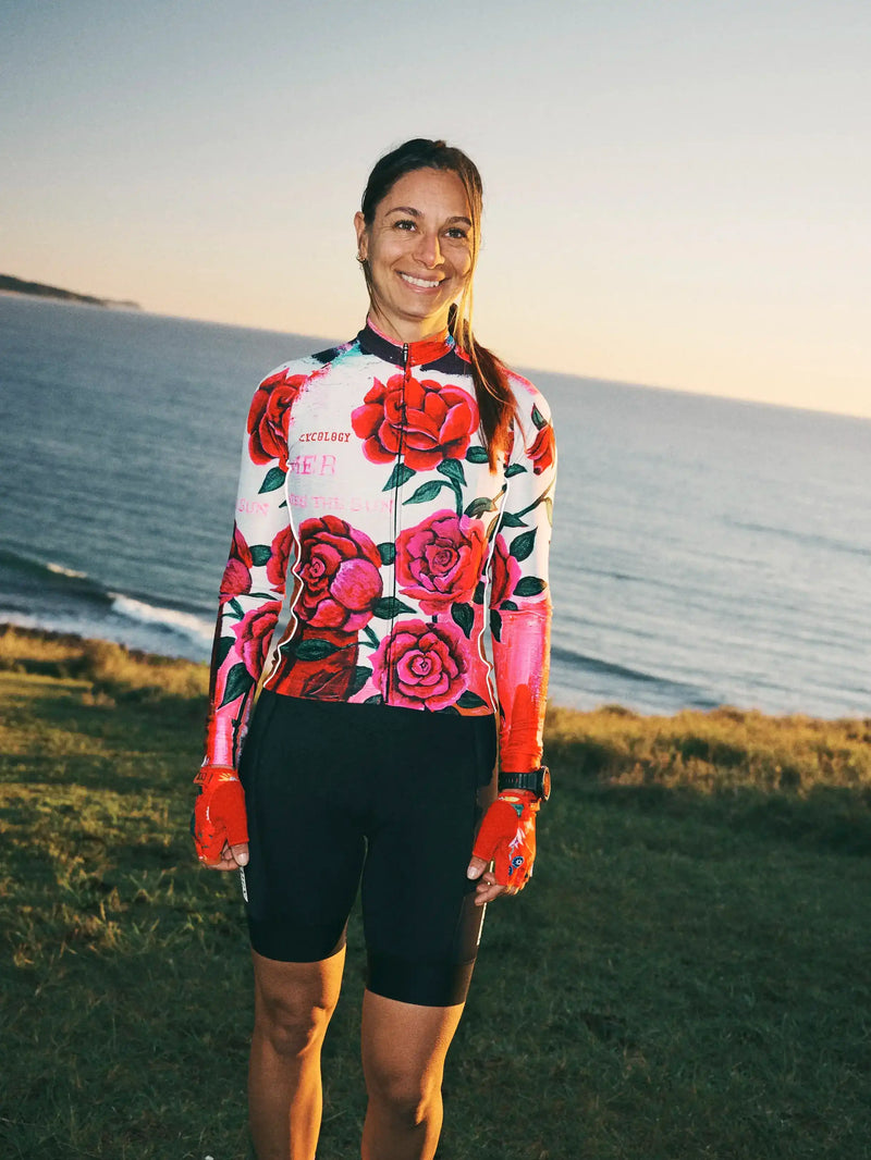 Woman in floral cycling jersey and black shorts, standing by ocean at sunset