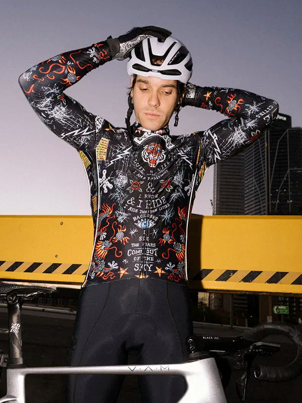 Person wearing a black winter cycling jersey with intricate designs and tiger cycling outfit with a helmet, standing in front of a yellow and black striped barrier.