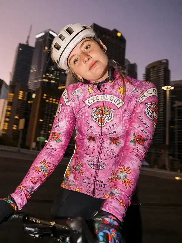 Woman in pink tiger-print cycling jersey riding bike in city at dusk, wearing helmet and gloves