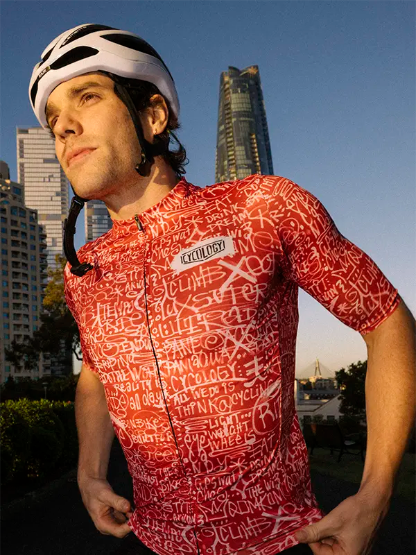 Person wearing a red cycling jersey with text and a helmet in an urban setting