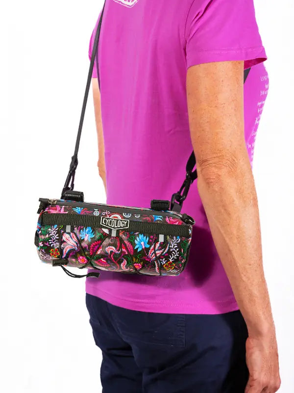Person wearing a pink shirt with a floral-patterned  bike bag over their shoulder.