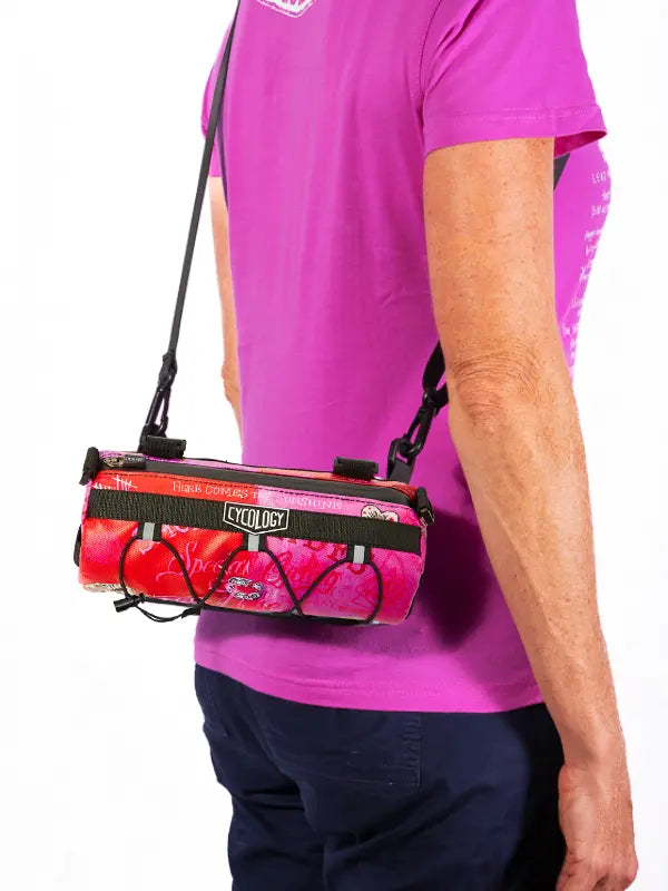 Person wearing a pink shirt with a pink and black bike bag on their shoulder