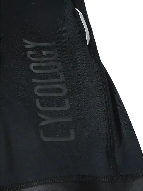 Close-up of a black Cycling bib leg with a large tonal vertical 'CYCLOLOGY' logo on the side and a small white reflective strip near the top.