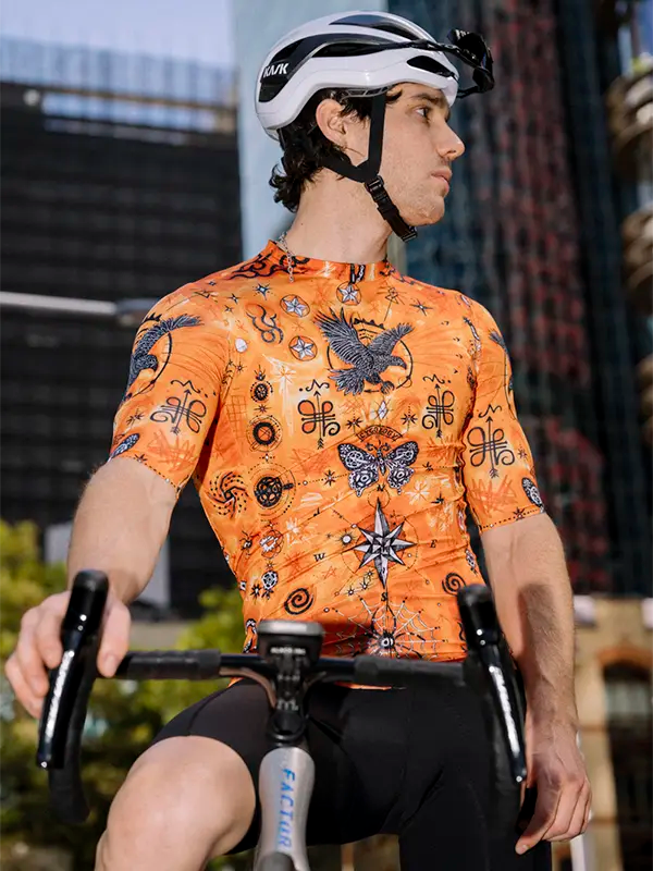 Person wearing an orange cycling jersey with tattoo style  design, sitting on a bicycle.