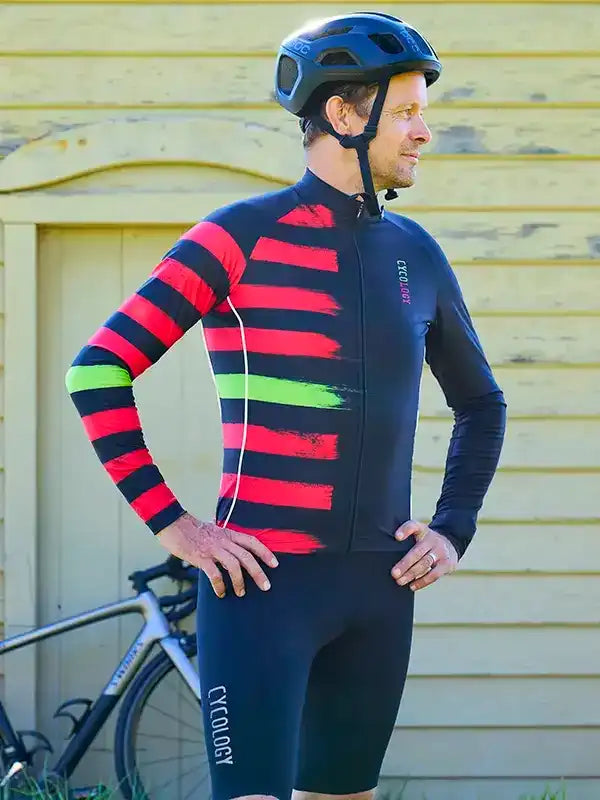 Man in red and black striped cycling jersey with green accents, wearing helmet, standing beside bike