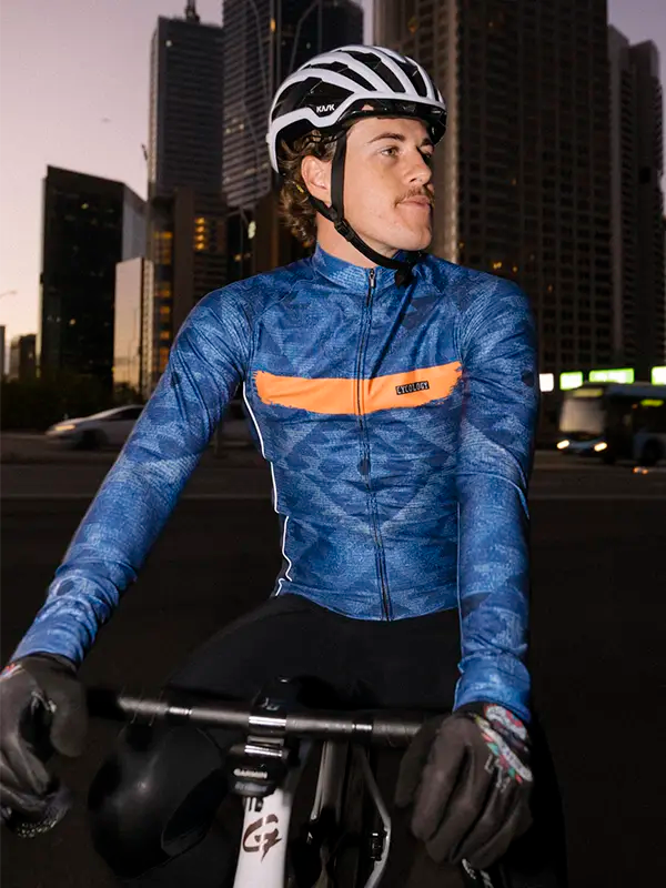 Cyclist in a blue long sleeve cycling jersey with an orange stripe in an urban setting