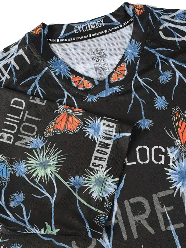 Black cycling jersey with butterfly and floral print, featuring 'BUILD NOT BREAK' text and breathable mesh fabric.