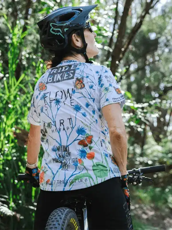Woman in floral cycling jersey and helmet on mountain bike trail, enjoying nature ride
