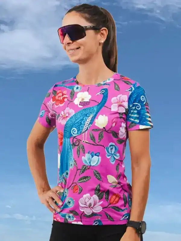 Woman wearing vibrant pink floral cycling jersey with peacock design, ideal for bike rides and outdoor adventures.