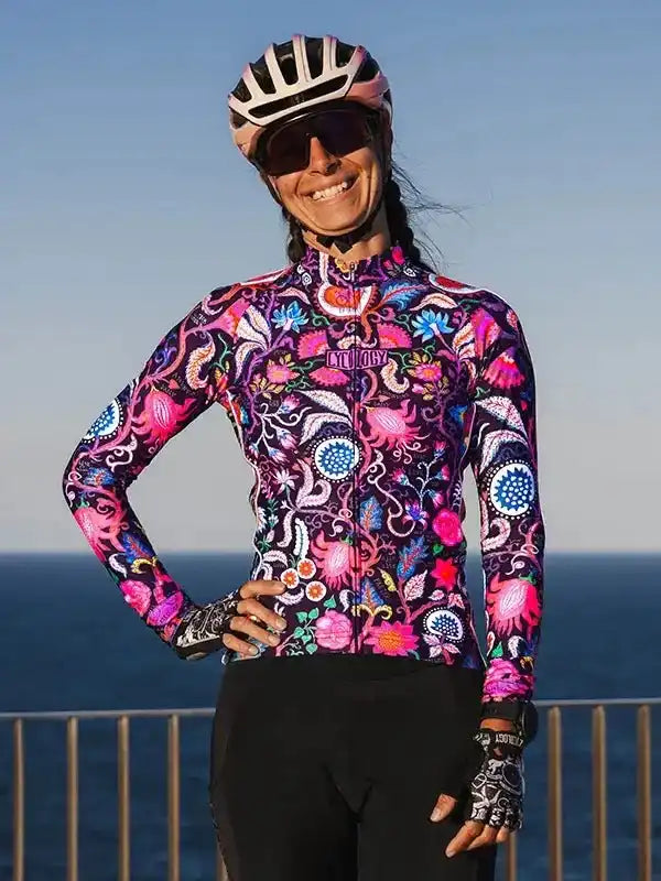 Woman in vibrant floral cycling jersey and helmet, ocean backdrop, stylish bike apparel