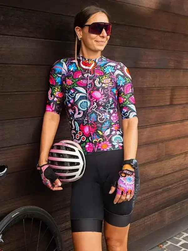 Woman in vibrant floral cycling jersey and black shorts, holding helmet, ready for ride