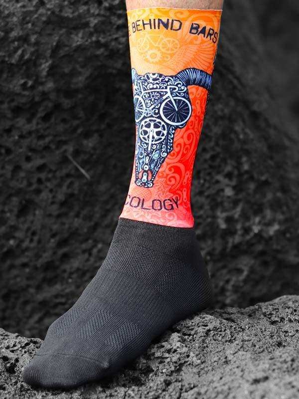 Cycling sock with bull skull and bike design, vibrant orange and red, worn on rocky terrain