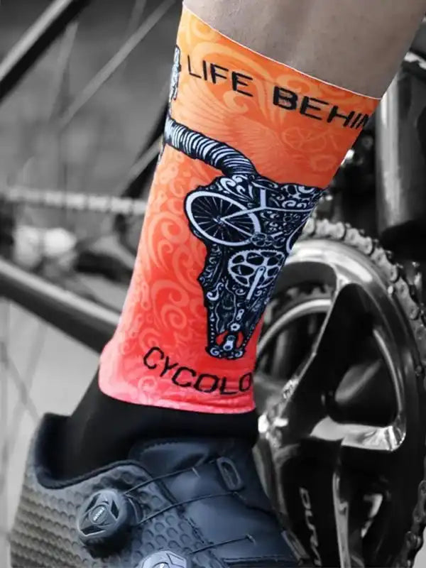 Vibrant orange cycling sock with skull & bike design, worn with clip-in shoe near bike gear