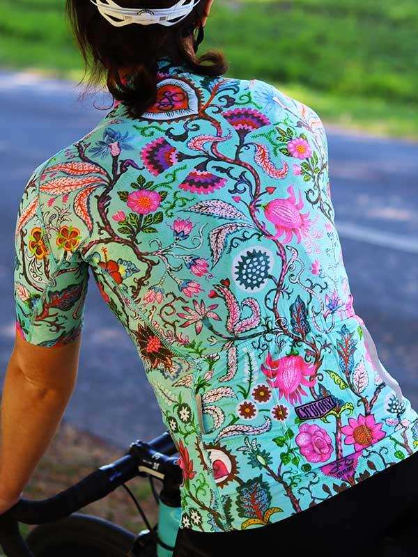 Woman cycling in vibrant floral print jersey, colorful botanical design on teal cycling apparel