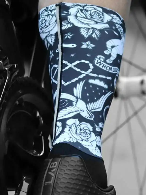 Cycling leg warmer with floral and bird tattoo-style design, worn with bike shoe