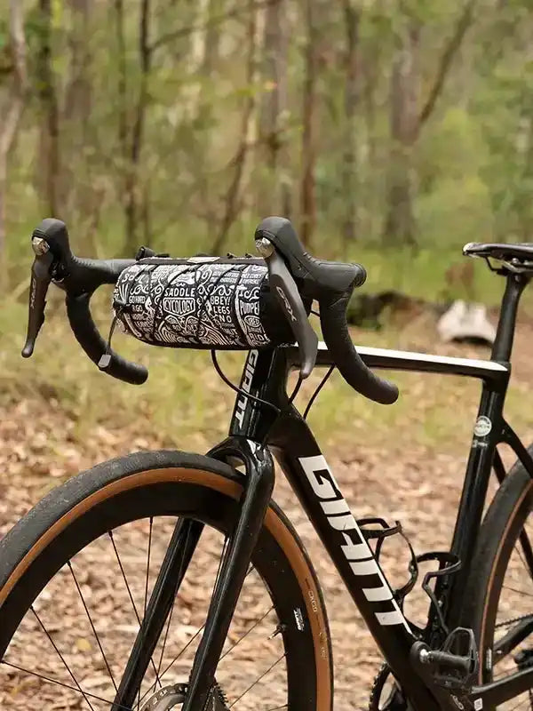 Black road bike with patterned handlebar bag in forest setting, ideal for cycling adventures